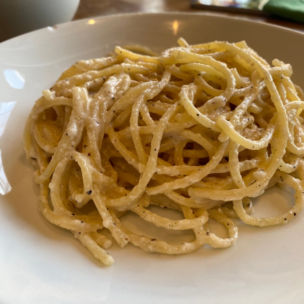 A shallow white bowl holds a tangle of spaghetti. It's coated in a slightly lumpy white cheese sauce with flecks of black pepper throughout.