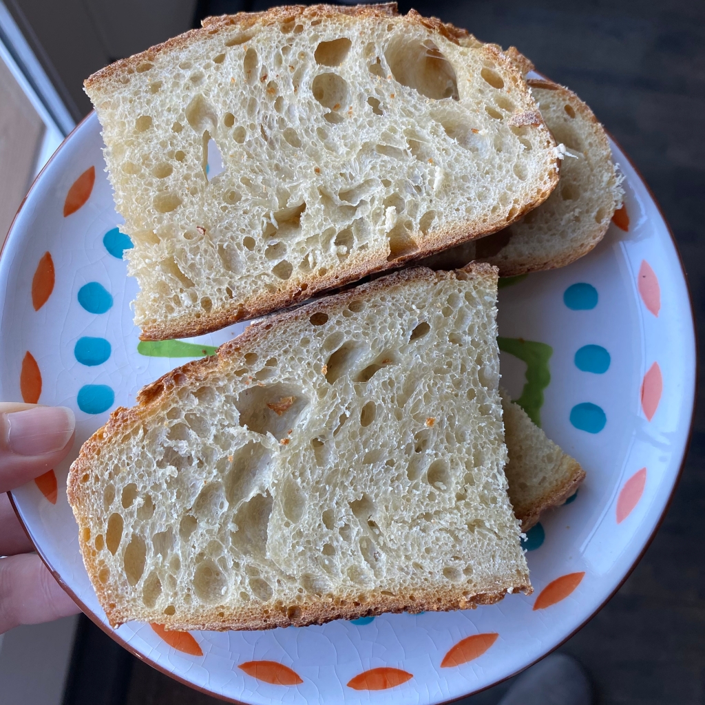 Four slices of white bread rest on a white plate with orange, teal, and green brushstrokes. The slices of bread are long pieces cut in half. They have a lot of holes in them of different sizes. They look delicious.