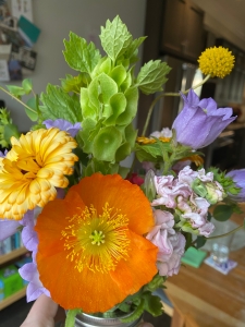 A bouquet with an orange poppy in full bloom, surrounded by yellow and purple flowers 