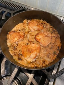 A black pot sits on a gas stove. It's filled with golden brown rice and crispy-looking chicken thighs.