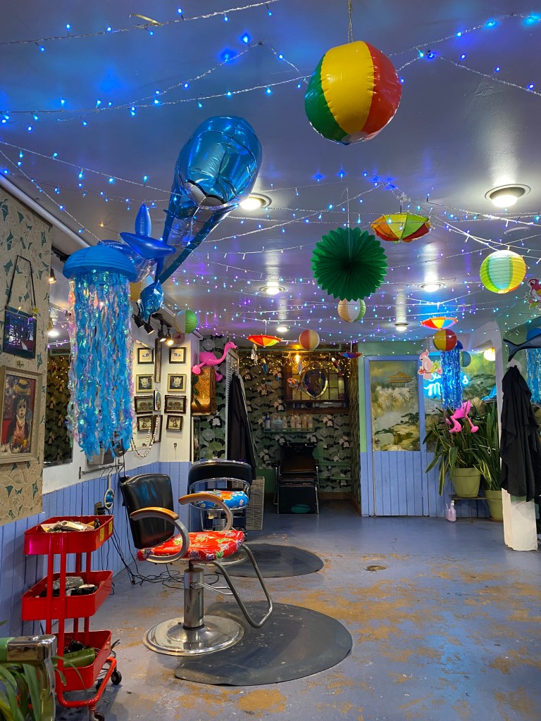 The interior of Saint Martin's Salon at the moment. Blue led string lights are crisscrossing the ceiling, interspersed with beach balls, upside down rainbow umbrellas, a dolphin balloon, and some huge paper jellyfish.