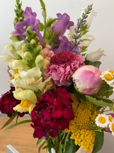 A bouquet of light yellow snapdragon, deep yellow yarrow, frothy pink adn red blooms, stems of lavendar and white bellflower, and some yellow and white feverfew, plus a pink peony bud.